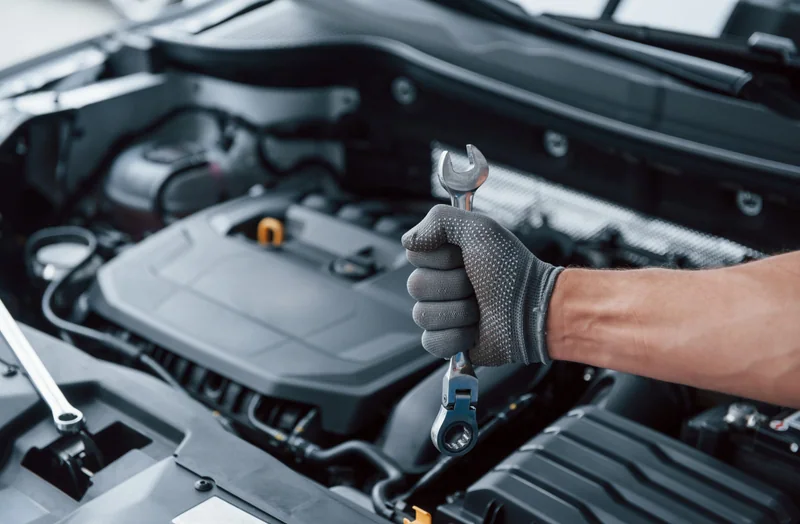 Hand mit Arbeitshandschuh und Schraubenschlüssel bei der Fahrzeugwartung